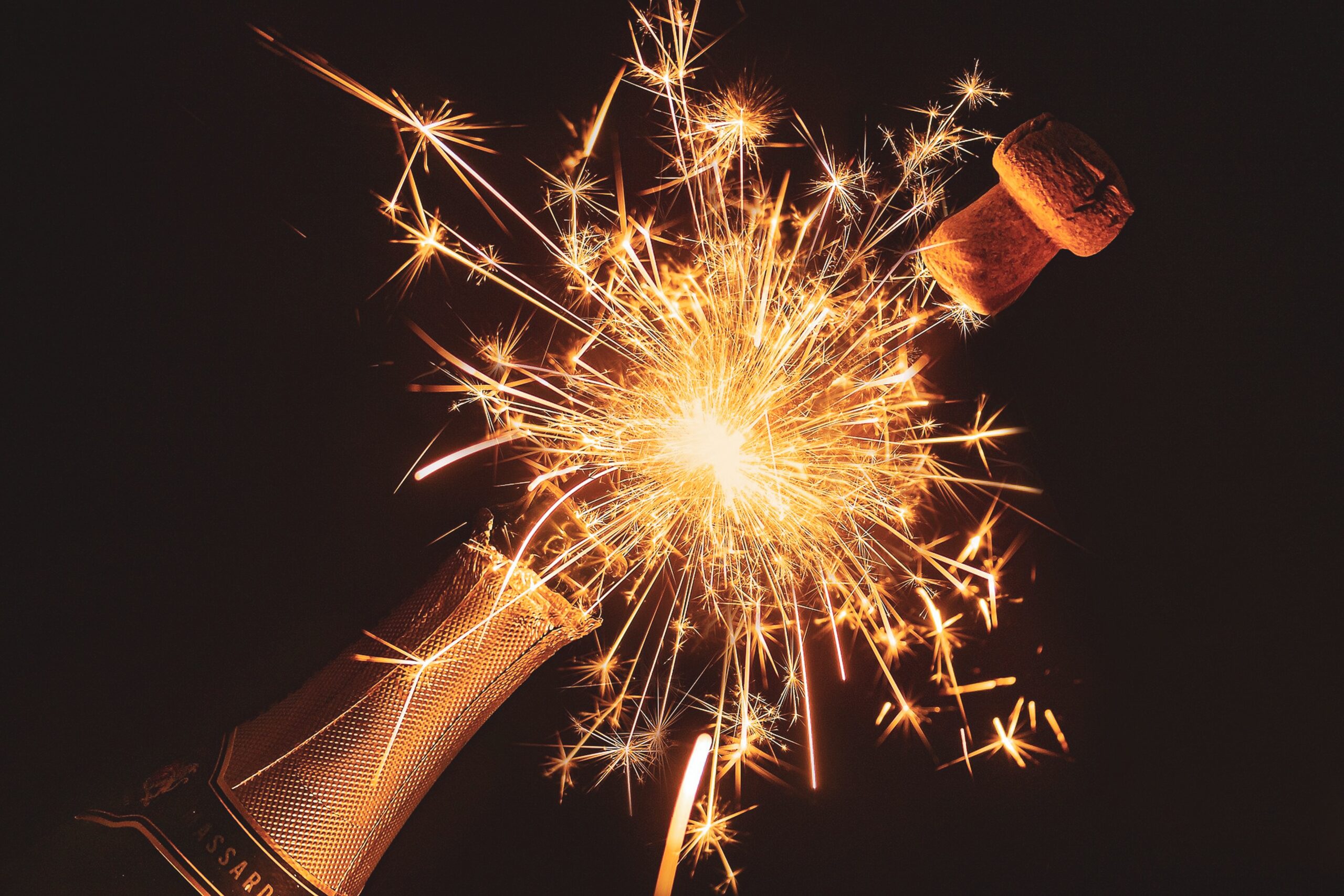 Champagne cork flying off a champagne bottle with a sparkler in between the cork and the bottle