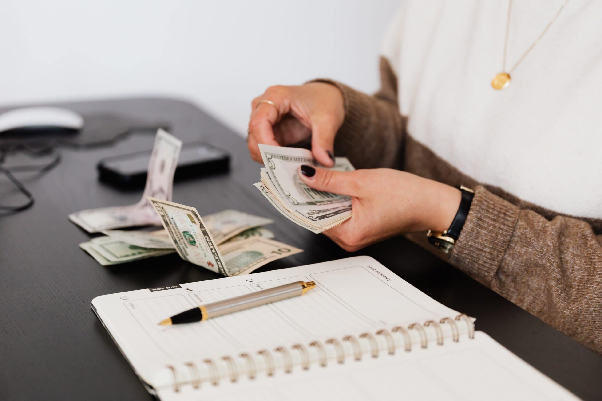 Person's hands counting out dollar bills next to a notebook.