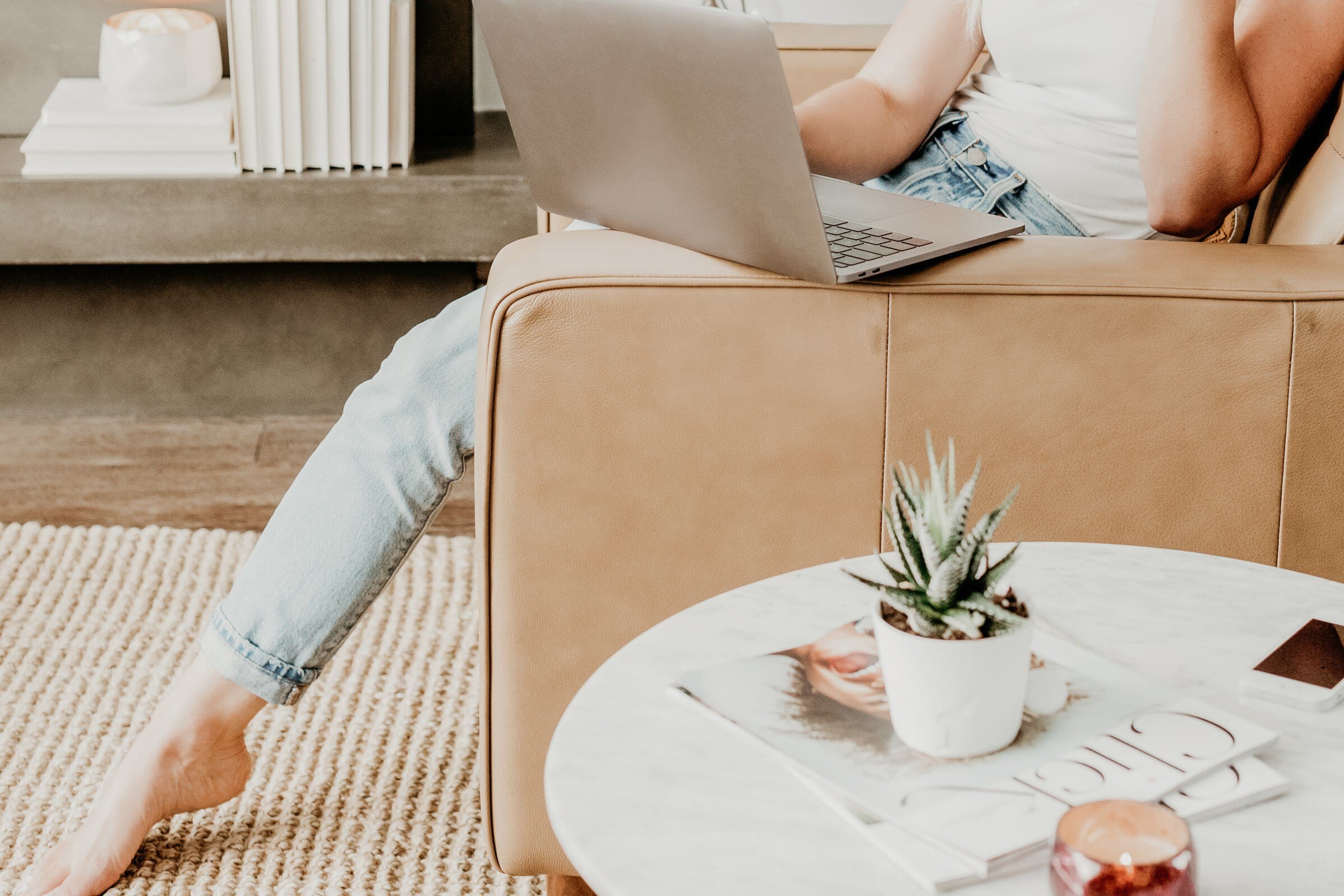 Woman sitting on a sofa, typing on a laptop.