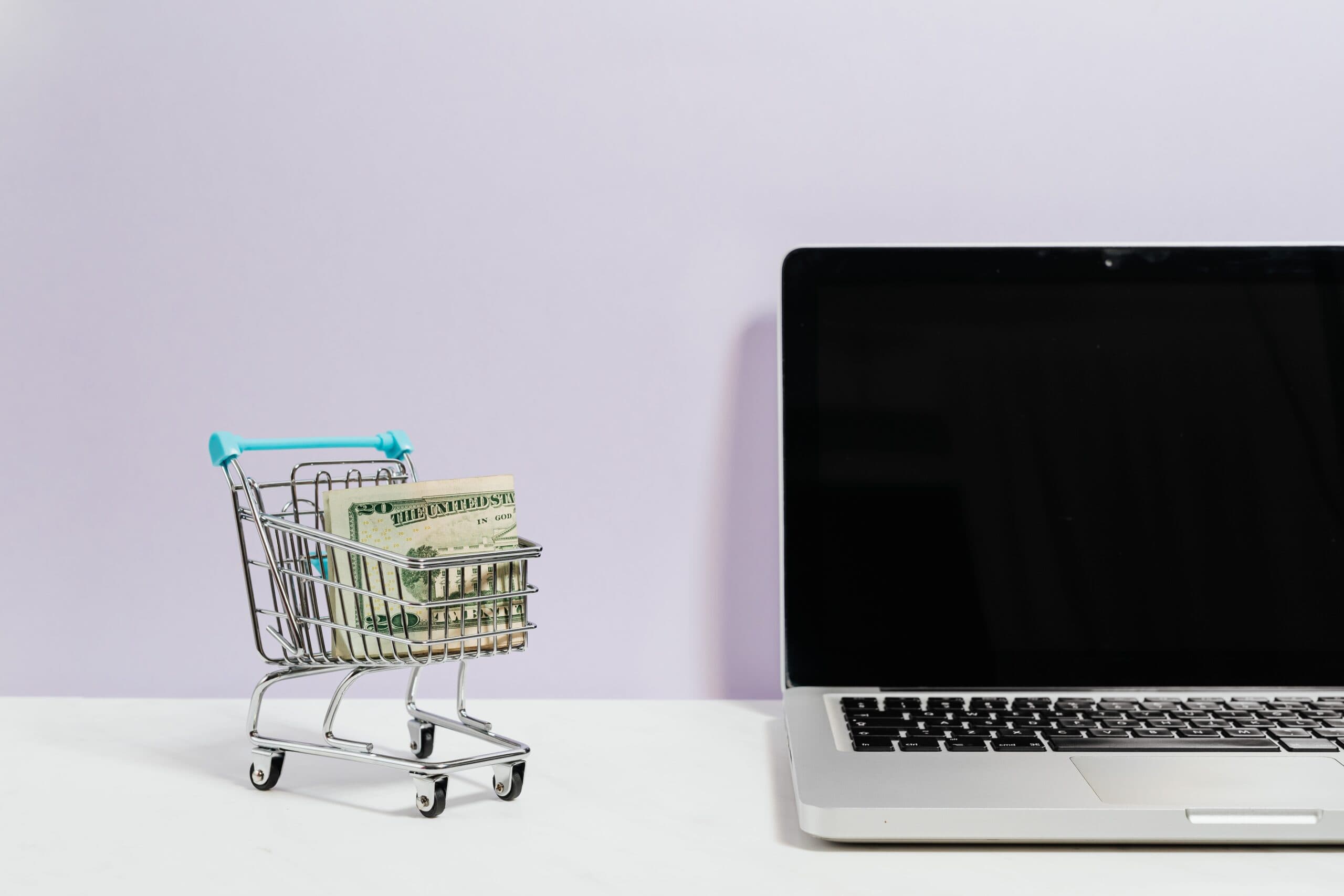 Miniature trolley containing dollar bills, next to a laptop.