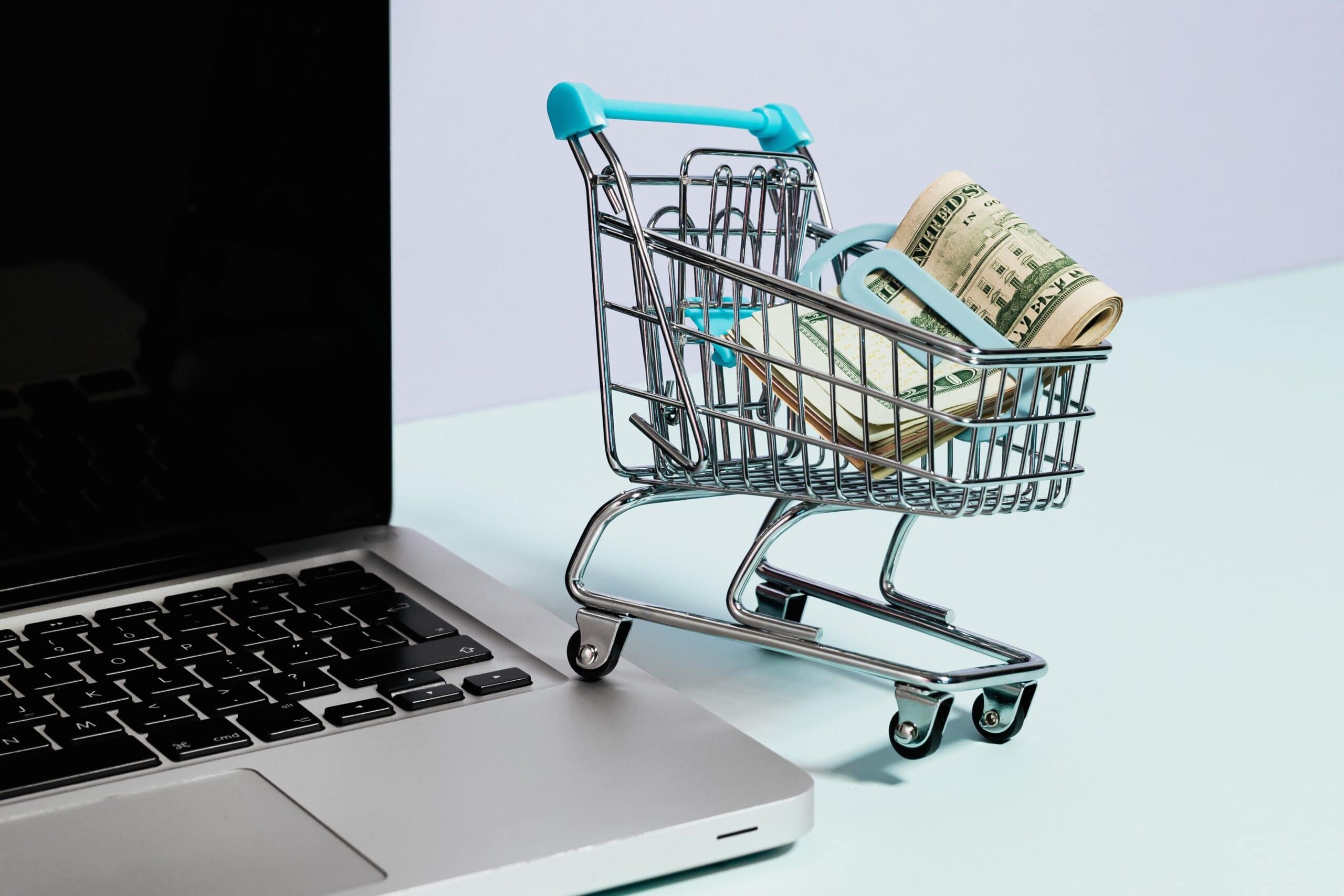 Miniature trolley containing dollar bills, resting on a laptop.