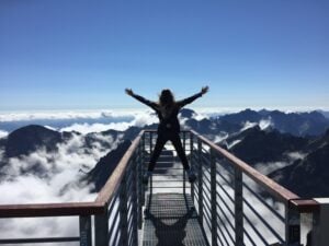 Person standing at the top of a mountain. Arms outstretched to celebrate the success.