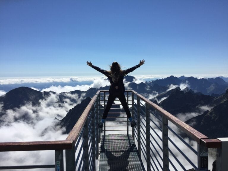 Person standing at the top of a mountain. Arms outstretched to celebrate the success.